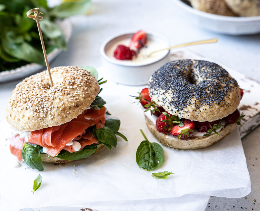 deux bagels sans gluten Piaf garnis. L'un est aux graines de sésame avec du saumon fumé et l'autre est aux graines de pavot avec des fraises.